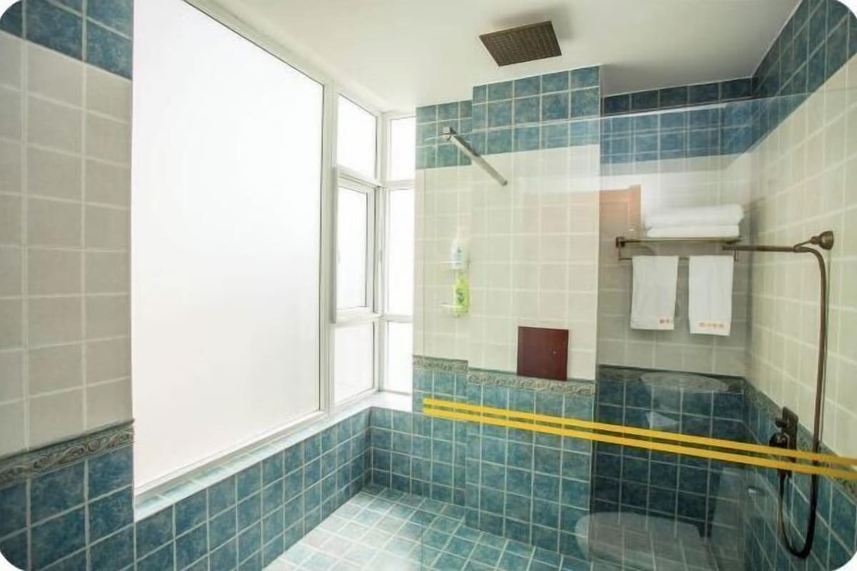 A bathroom with blue tiles, a glass shower enclosure, a window, and a towel rack with towels.