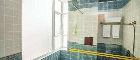 A bathroom with blue tiles, a glass shower enclosure, a window, and a towel rack with towels.