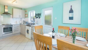 A modern kitchen with white cabinets, a built-in oven, a washing machine, and a dining area with a wooden table set for two. - Cwtch Cottage, Holiday Cottage Broad Haven, Sleeps 5, 3 bedrooms,  bathrooms (Haverfordwest)