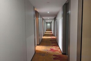 A hotel corridor with a carpeted floor and a series of doors on one side. - Tiansheng Hotel (Ningbo Lishe Airport) (Ningbo)