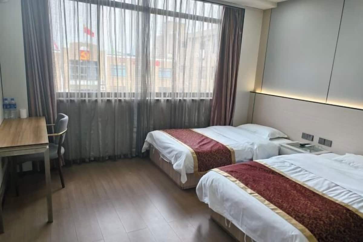 Une chambre d’hôtel avec deux lits, un bureau en bois, une chaise, une table de chevet et une fenêtre avec des rideaux.