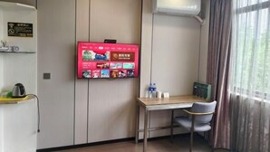 Een hotelkamer met een wandtelevisie waarop verschillende programma’s te zien zijn, een bureau met een stoel en een airconditioning.