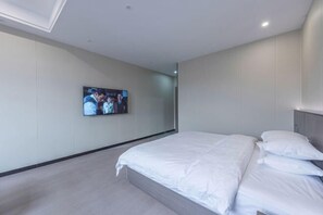 Una camera d'albergo moderna con un ampio letto, una TV a schermo piatto fissata al muro e un design minimalista.