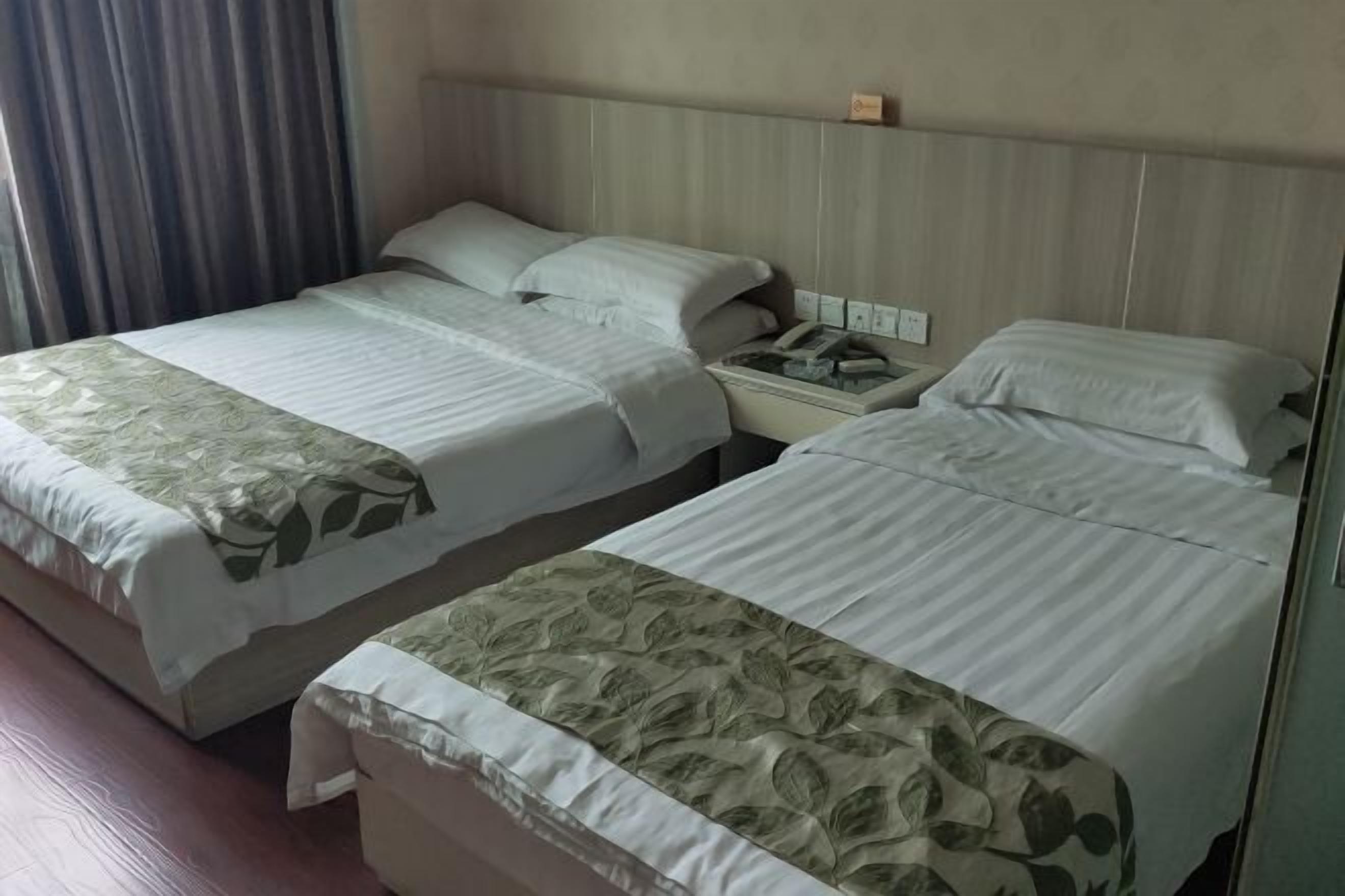 Two twin beds with floral bedspreads, a bedside table with a phone, and a wall-mounted light fixture.