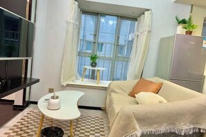 A small, neatly arranged room with a bed, a TV, a small table with a tissue box, a window with curtains, and a refrigerator. - City Posthouse (Shenzhen Buji Daduhui) (Shenzhen)
