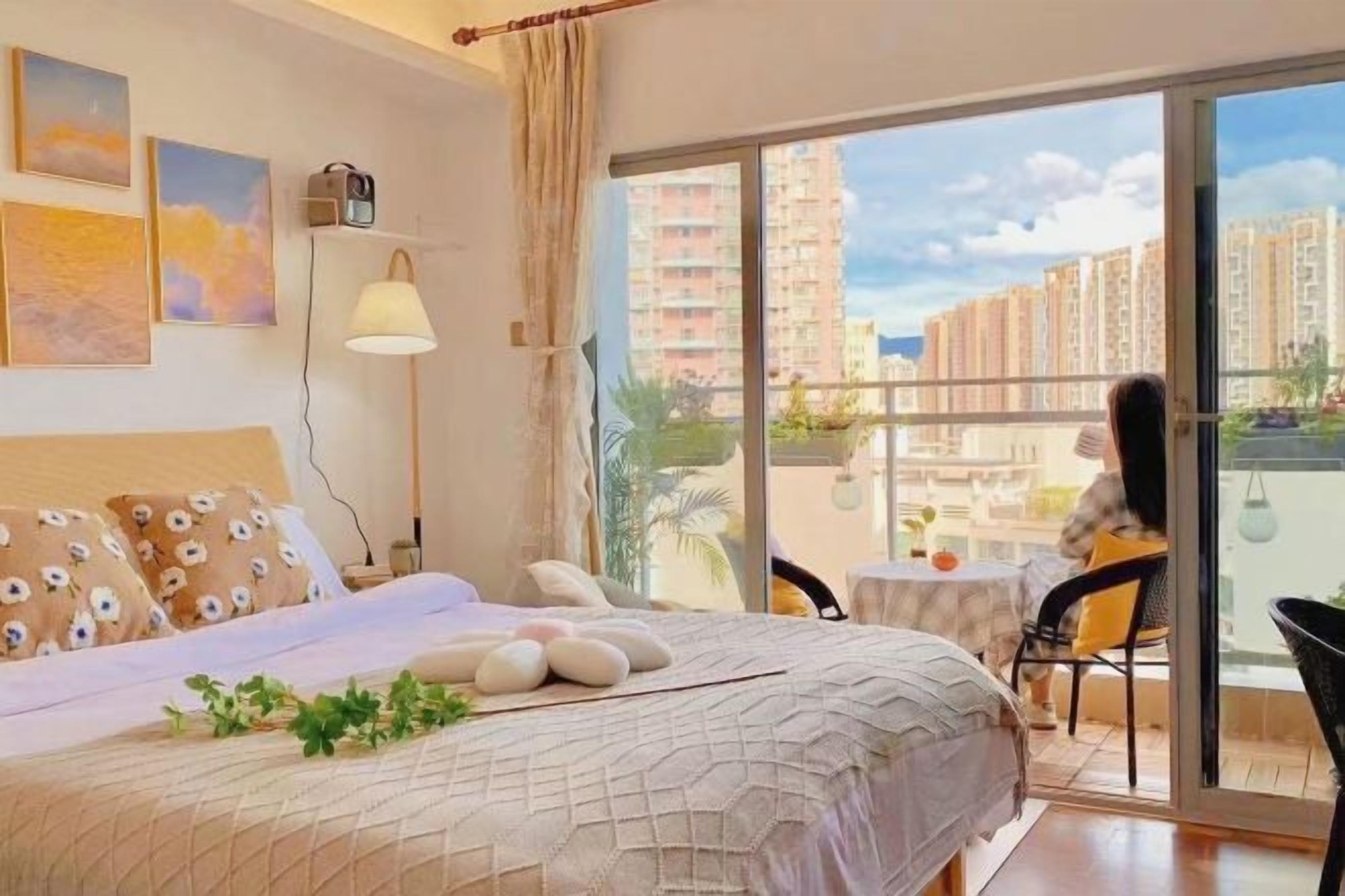 A bedroom with a bed, a bedside table, a lamp, and a view of a balcony with a chair.