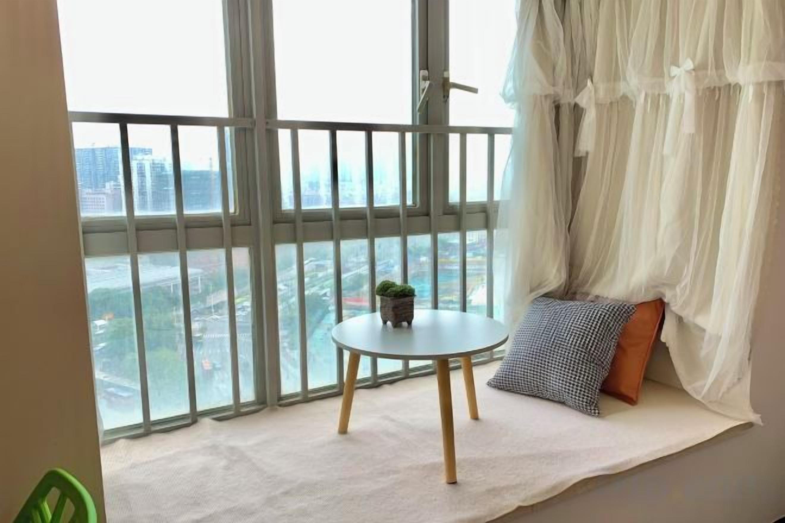 A balcony with a view of a cityscape, a small round table with a plant, and a white cushioned bench with pillows.