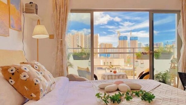 A hotel room with a large bed, a view of the city through floor-to-ceiling windows, and a small balcony with a table and chairs. - City Posthouse (Shenzhen Buji Daduhui) (Shenzhen)