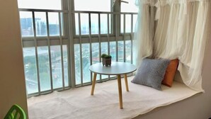 A balcony with a view of a cityscape, a small round table with a plant, and a cushioned seating area with a patterned pillow. - City Posthouse (Shenzhen Buji Daduhui) (Shenzhen)
