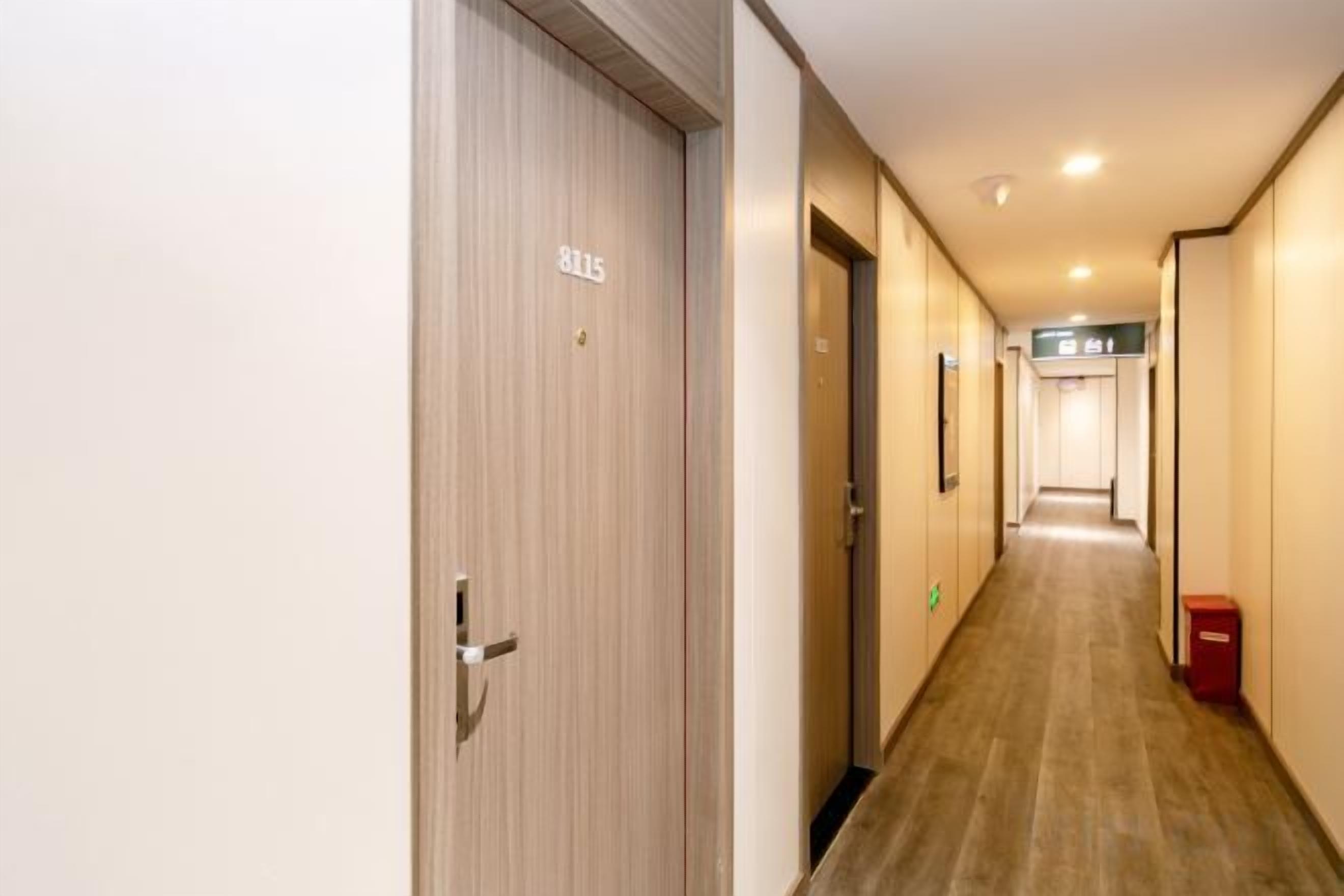 A hotel hallway with a wooden floor, a door marked '8015', and a trash bin on the right.