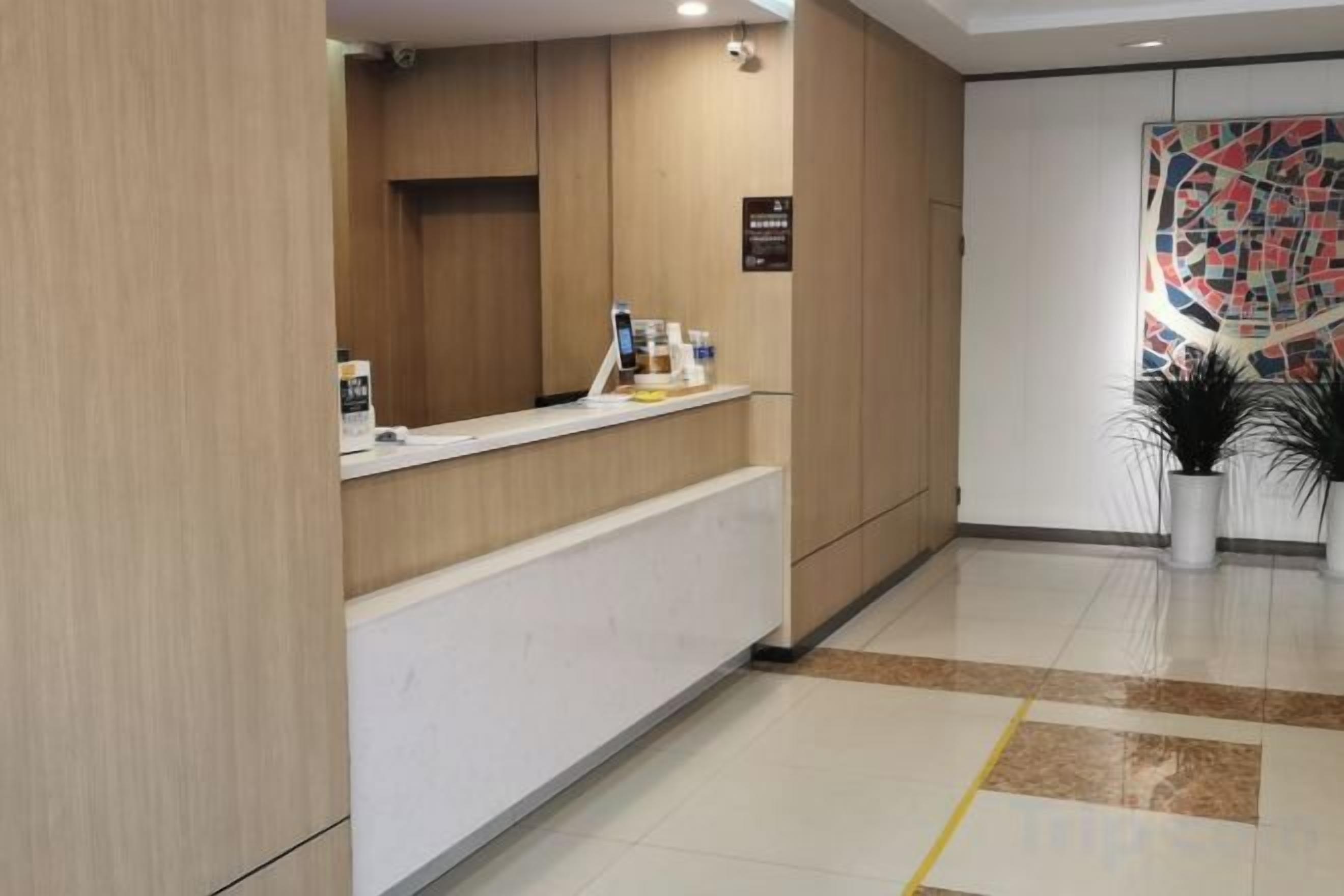 A reception desk with a white counter and a sign above it. There is a potted plant to the right of the desk.
