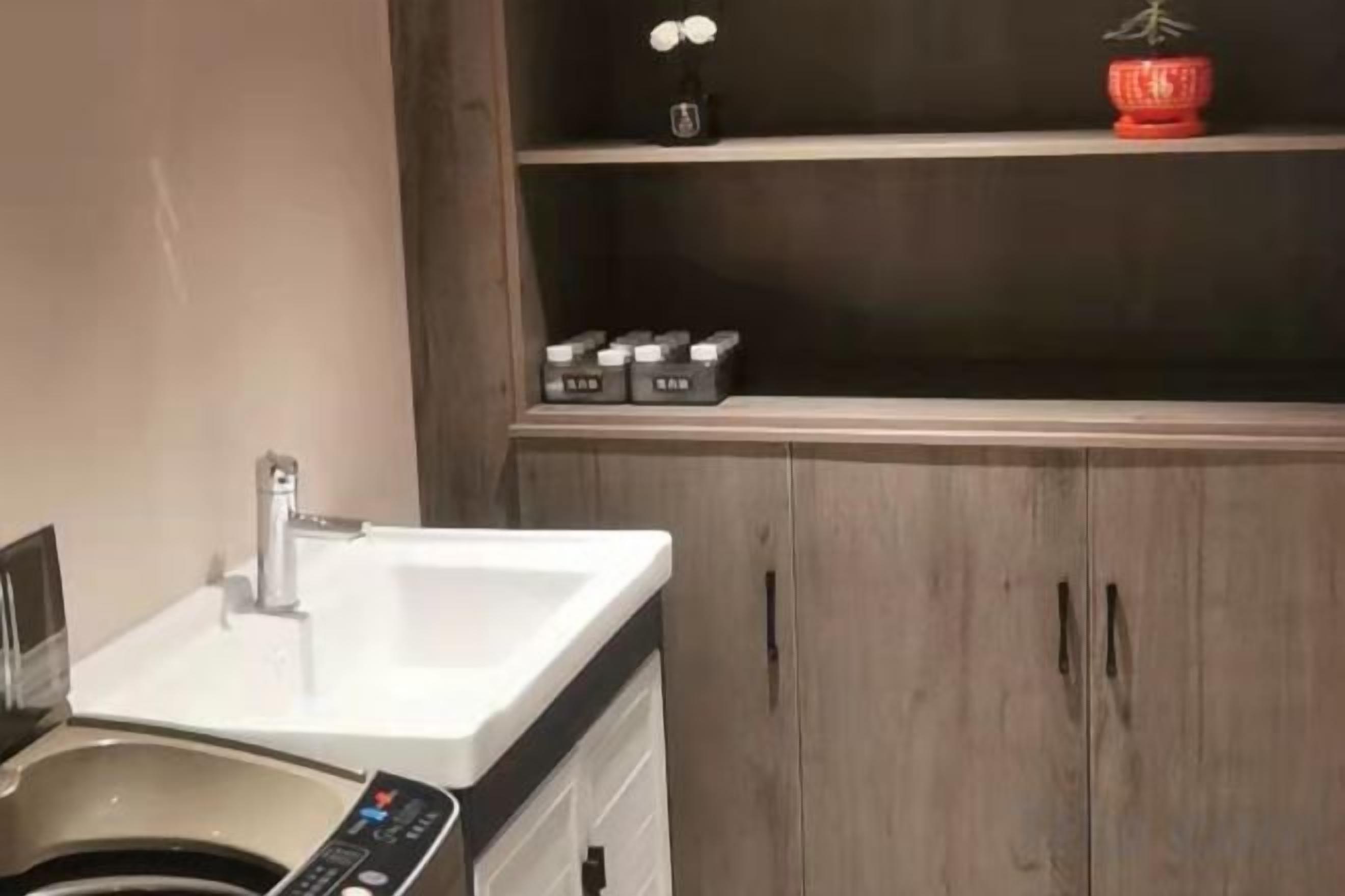 Un bagno con un lavandino bianco, una lavatrice e un mobiletto in legno con ripiano soprastante.