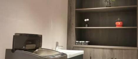 A kitchen with a built-in coffee machine, a sink, and a wooden cabinet with shelves.