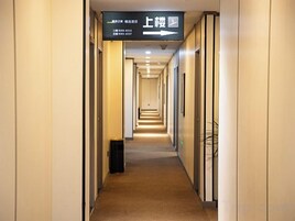 Un pasillo de hotel con señales de dirección, un cesto de basura y una planta.