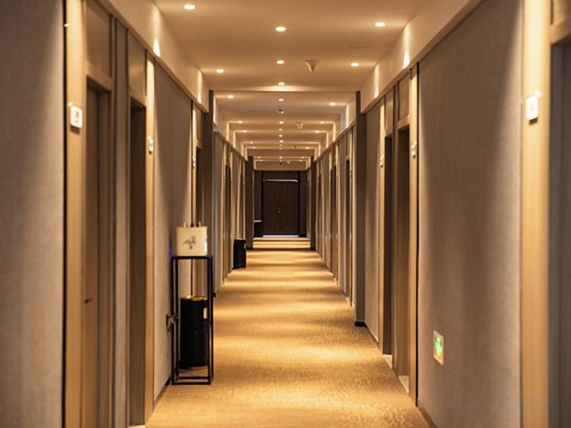 Un couloir d’hôtel avec des portes des deux côtés, un sol recouvert de moquette et un éclairage au plafond.