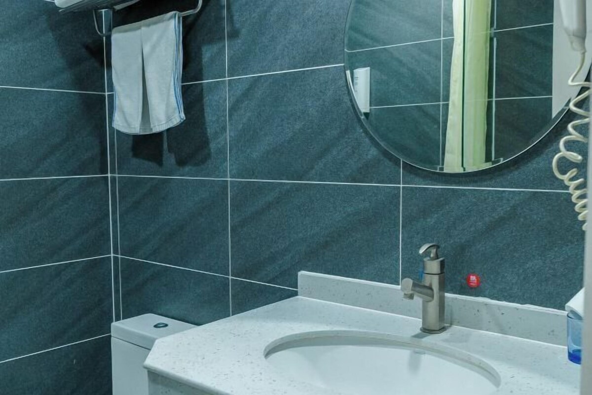 Un baño con baldosas oscuras, un lavamanos blanco, un espejo y una toalla colgada en la pared.