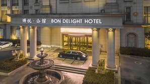 L’extérieur de l’hôtel BON DELIGHT présente une fontaine, des colonnes et une voiture garée devant.