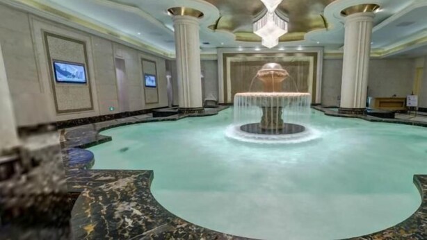A large indoor pool with a central fountain, surrounded by marble flooring and columns. - Bon Delight Hotel (Hefei)