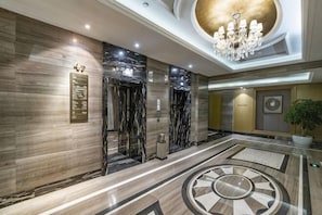 Eine Hotellobby mit Marmorboden, Aufzügen, einer Kristallleuchtre und einem großen, runden Muster auf dem Boden.