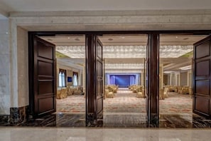 Hall d'albergo con pavimento in marmo, ampia area salotto con tavoli e sedie rotonde e uno sfondo a tenda blu.
