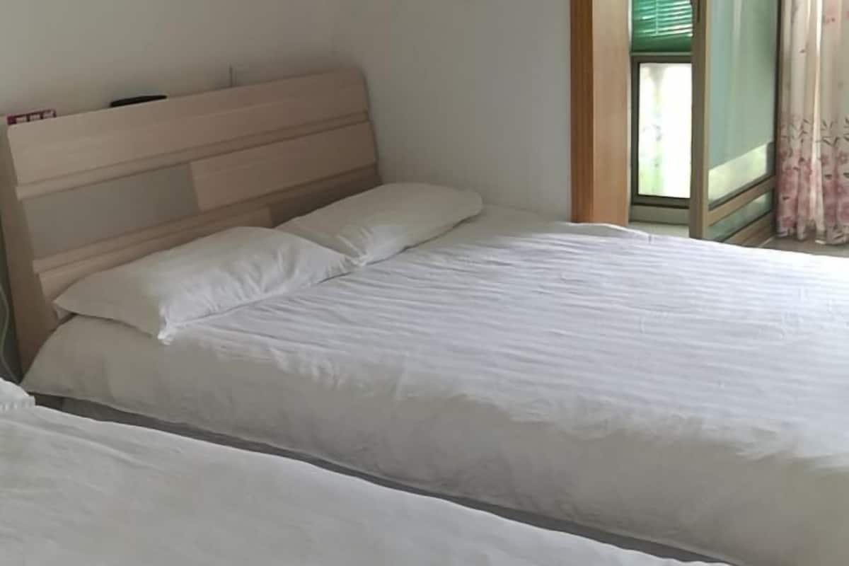 Una cama individual con cabecera de madera, ropa de cama blanca y una ventana con persianas verdes.