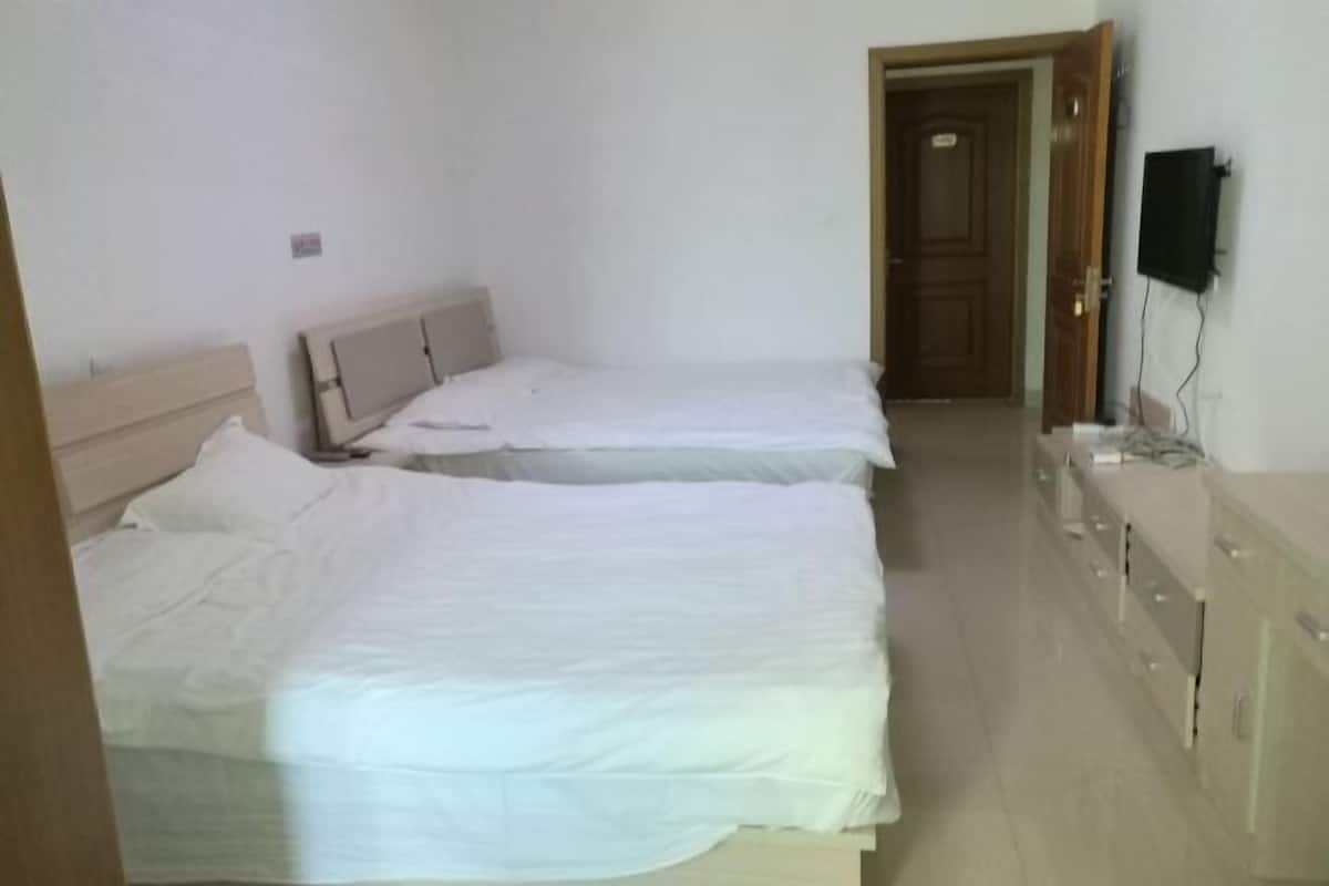 Una habitación con dos camas individuales, un armario de madera y un televisor en la pared.