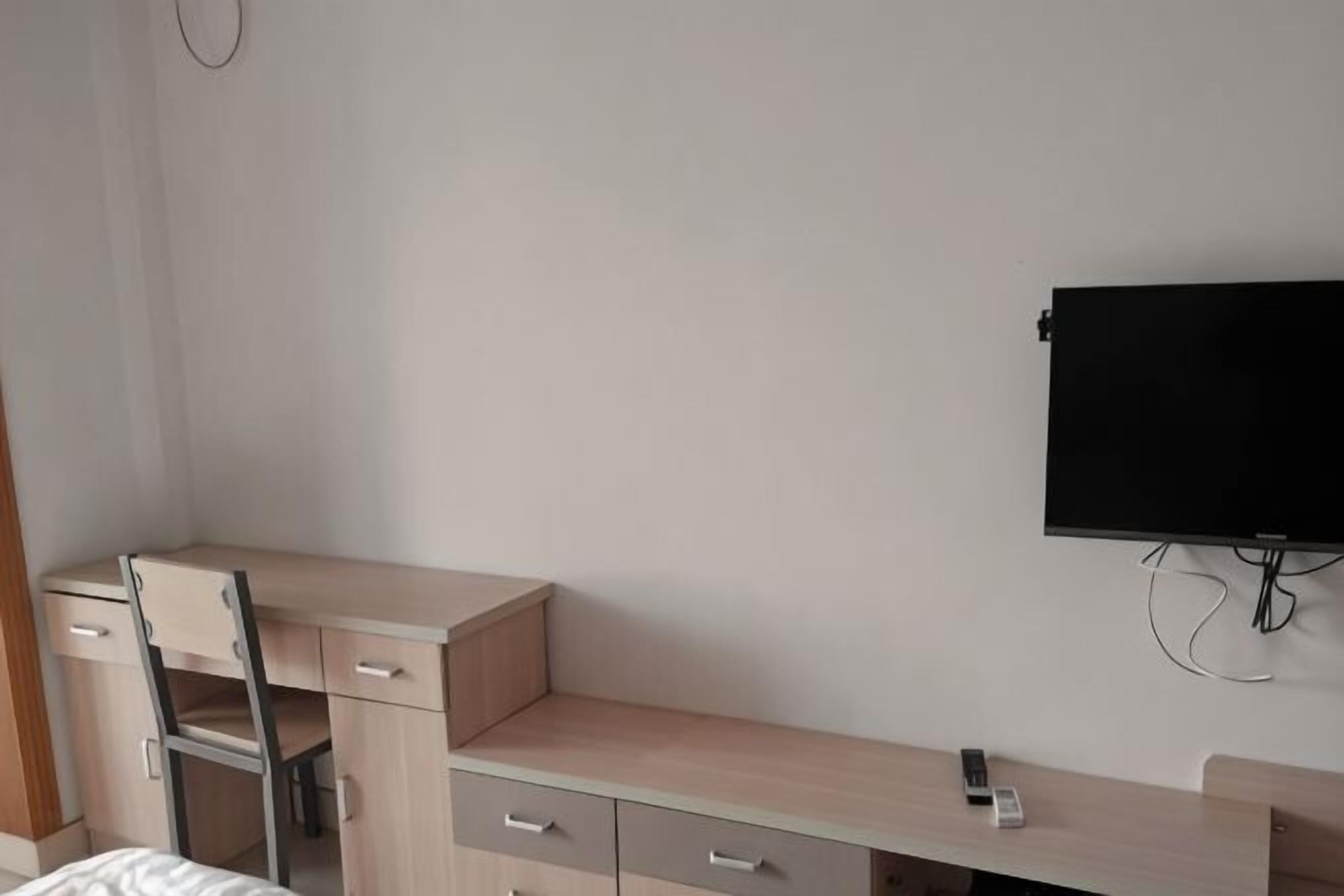 Ett sovrum med en säng, ett skrivbord, en stol och en tv som är monterad på väggen.
