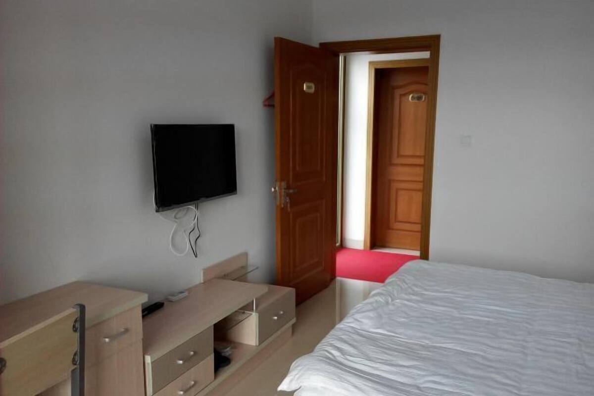 Un dormitorio con cama, televisor montado en la pared, puerta de madera y escritorio con cajones.