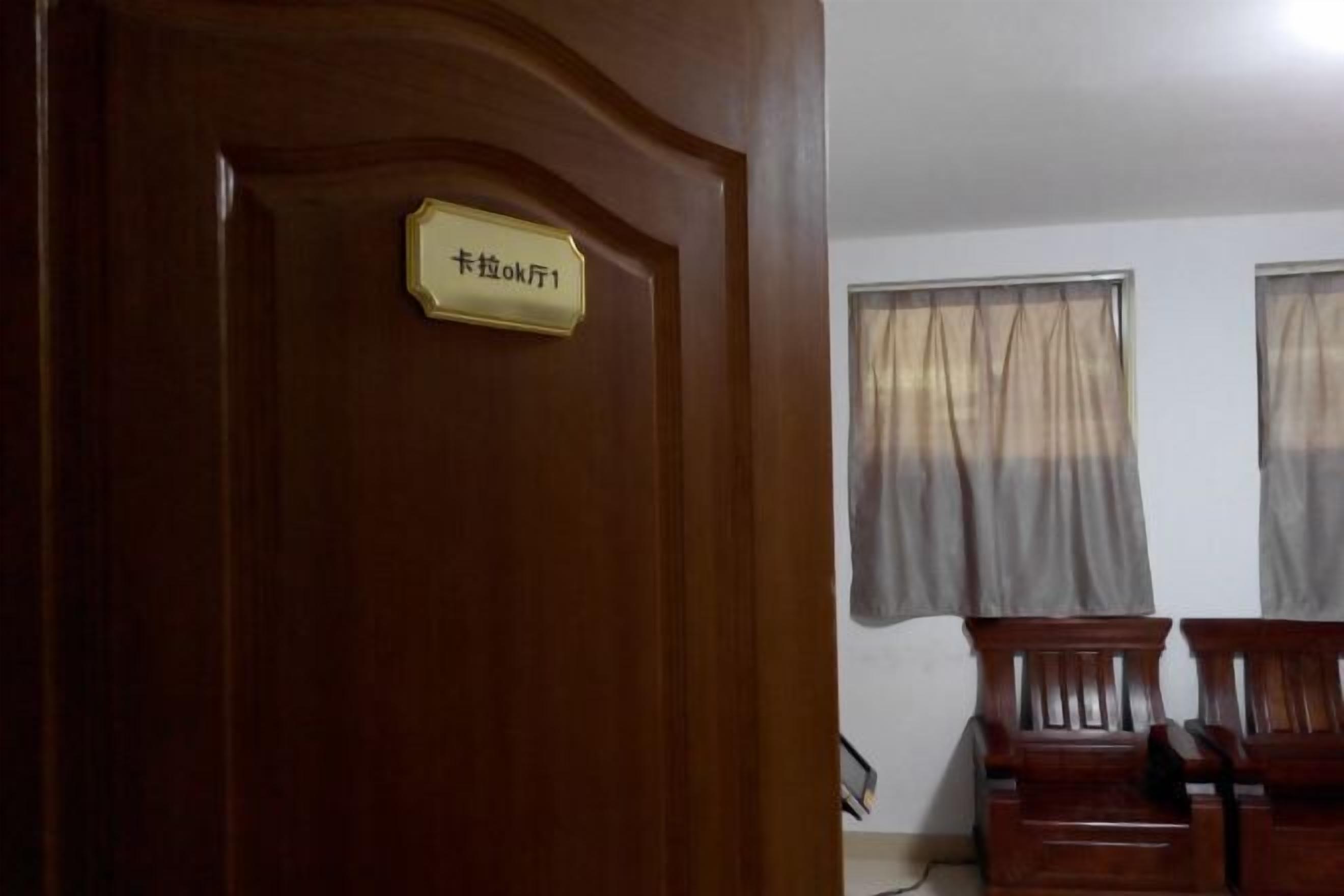 A wooden door with a sign, two windows with curtains, and two wooden chairs.