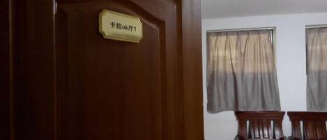 A wooden door with a sign, two windows with curtains, and two wooden chairs.
