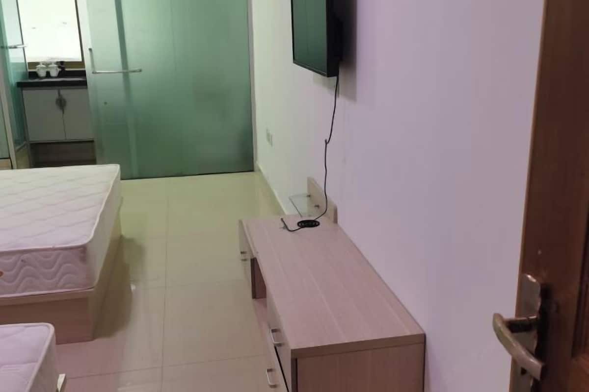 Una habitación con una cama, una mesita de noche de madera, un televisor montado en la pared y una puerta.