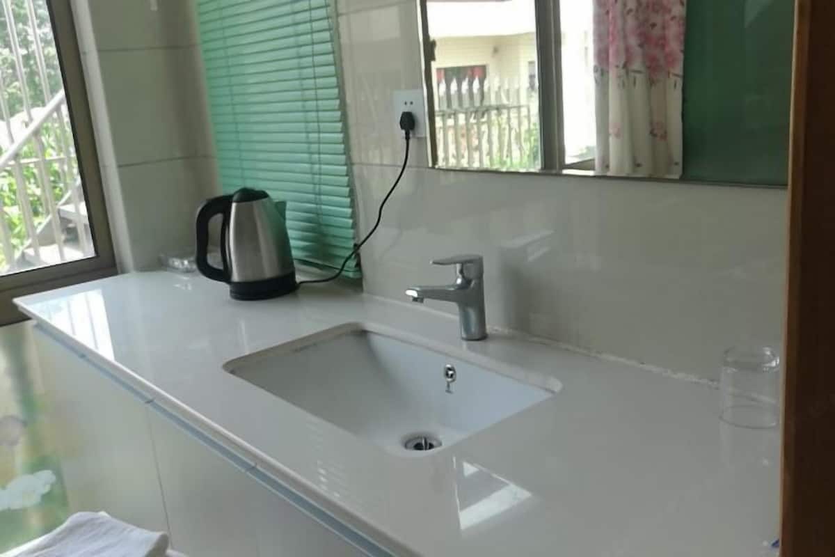 Una cocina moderna con un lavamanos blanco, hervidor de acero inoxidable y una ventana con persianas.