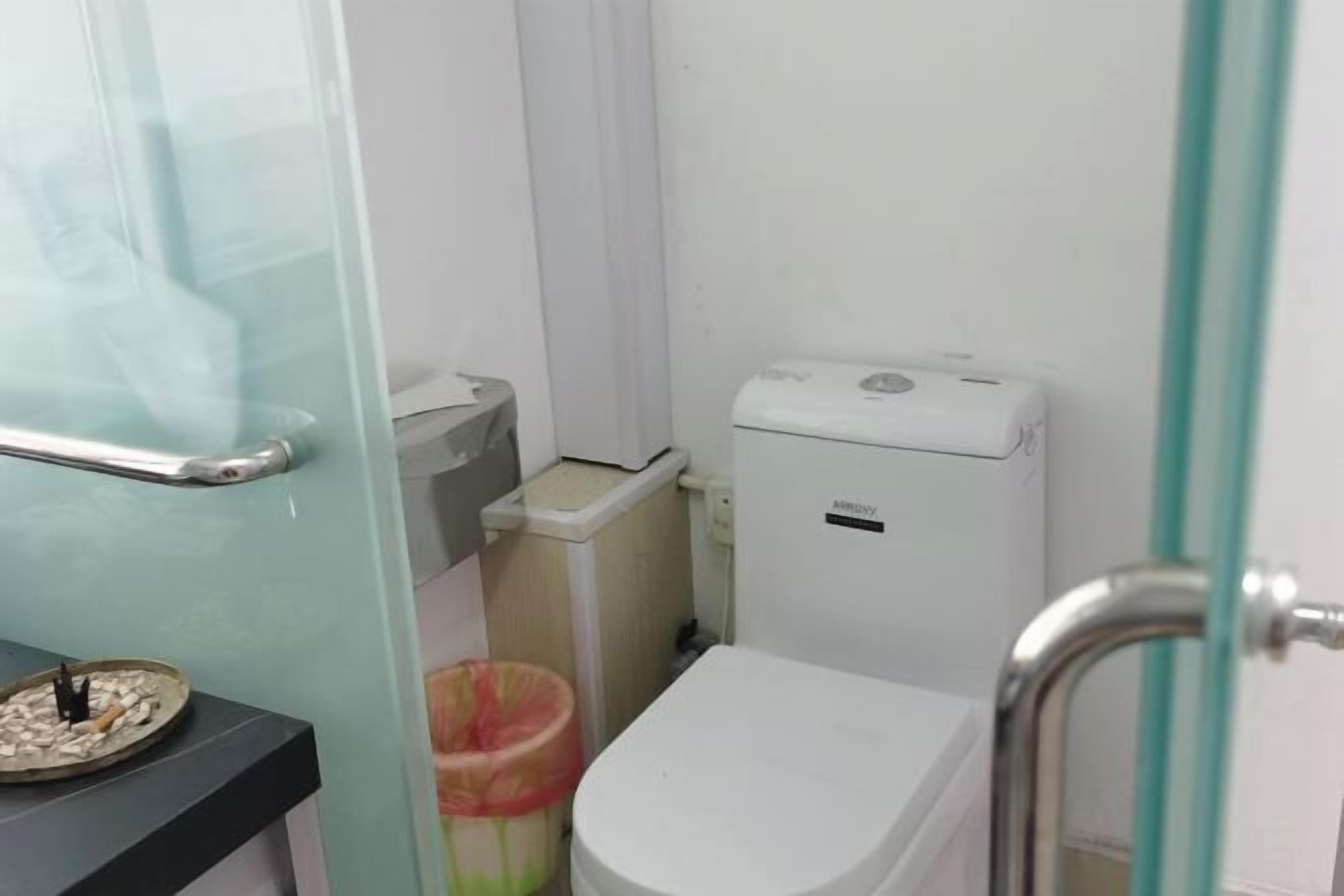 A bathroom with a toilet, a trash bin, and a glass partition.
