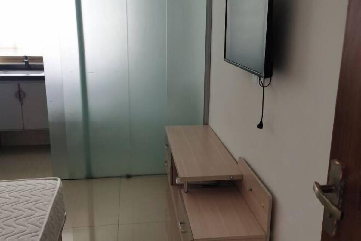 Una habitación con una cama, un banco de madera, un televisor montado en la pared y una puerta.