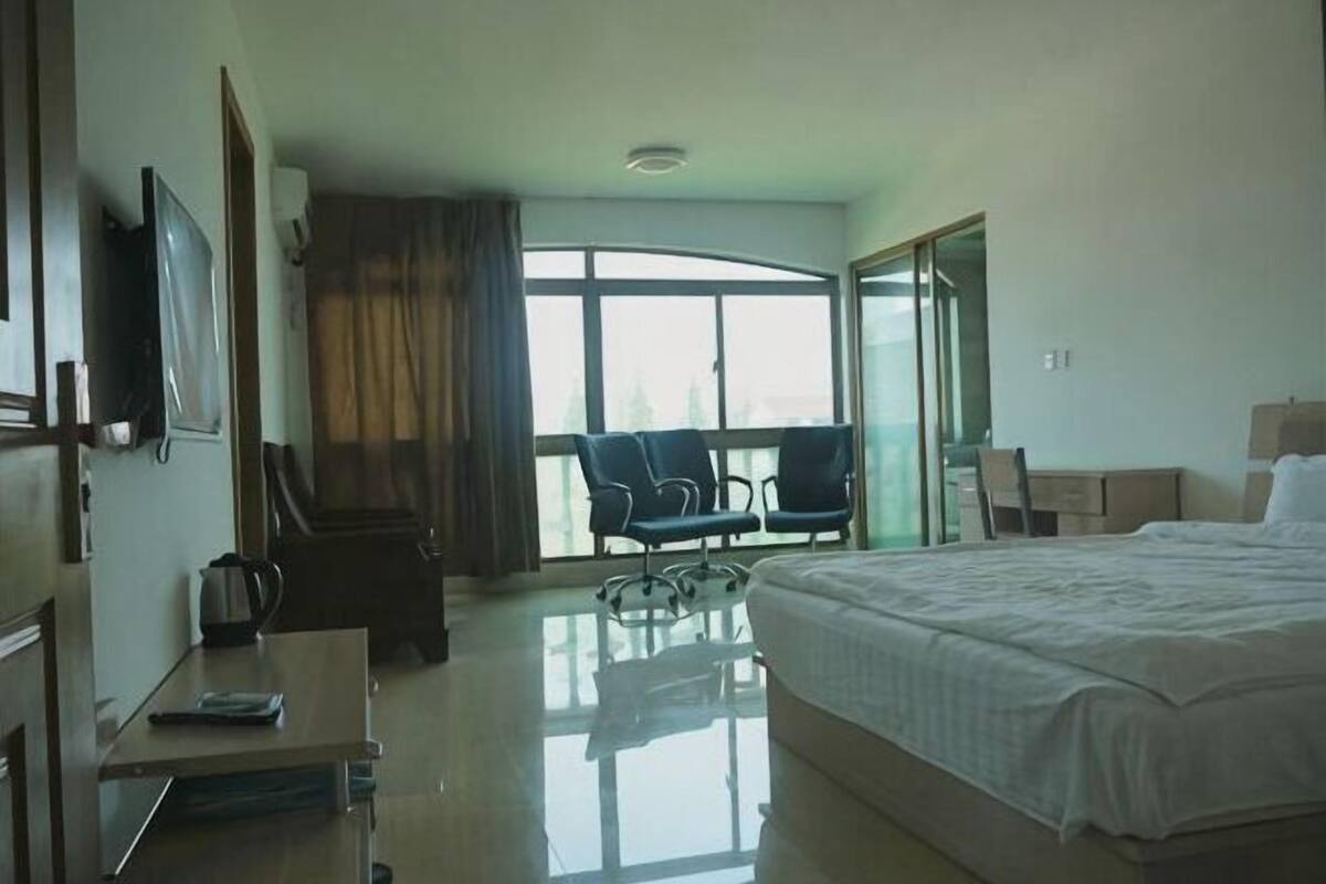 Una habitación de hotel con cama, escritorio, silla, televisor y un ventanal grande.