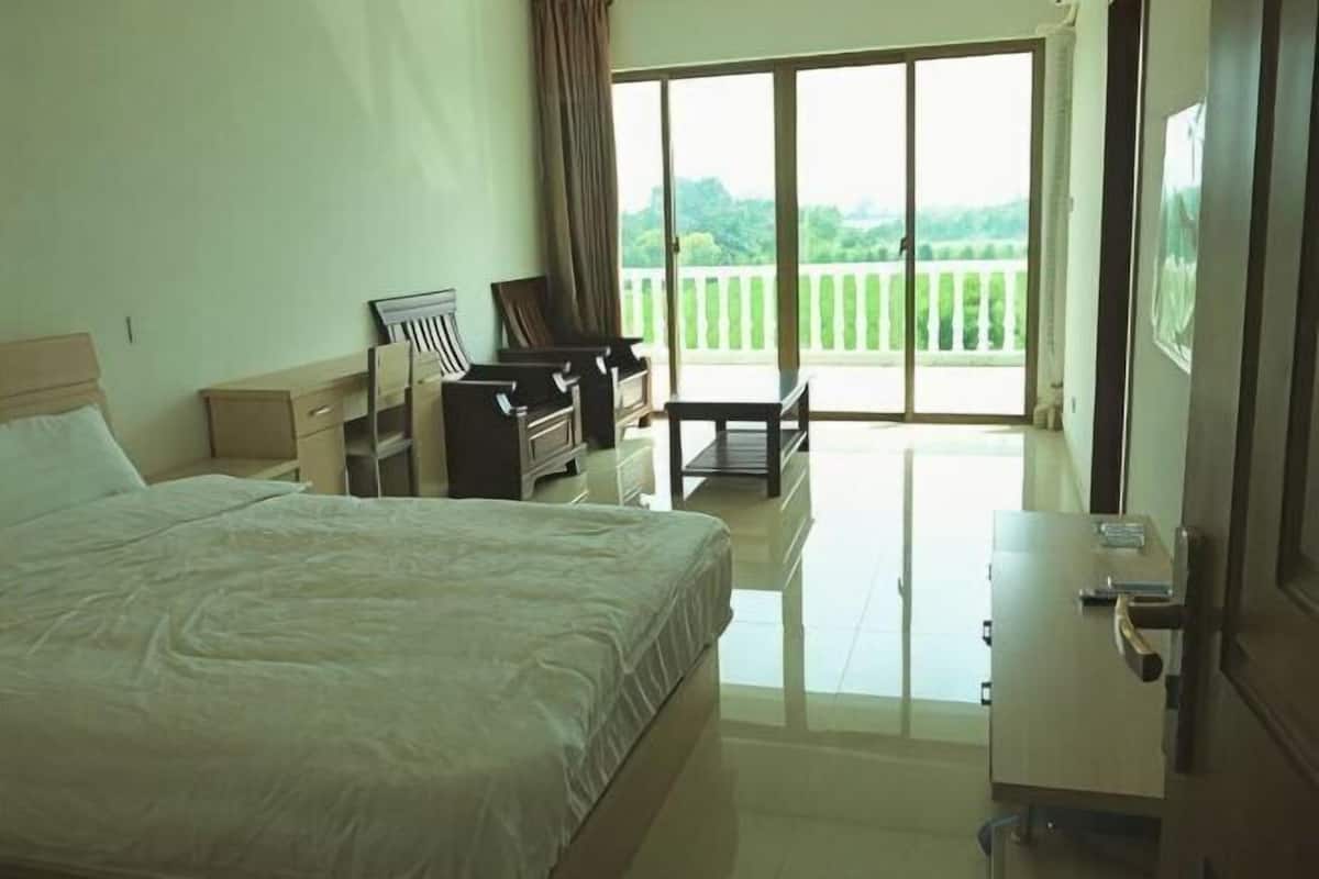 Habitación de hotel con cama, escritorio, silla, armario y balcón con vistas.
