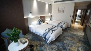 A hotel room with two beds, a small table with a plant, and a patterned carpet. - Chengcheng Huayuan Building (Chengcheng)