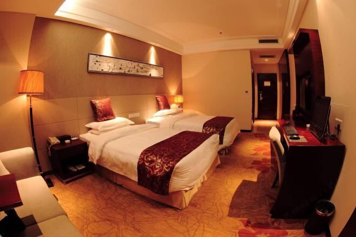 Ein Hotelzimmer mit zwei Betten, einem Schreibtisch, einem Sessel, einem Fernseher und einer Lampe.