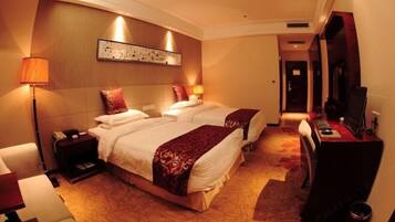 A hotel room with two beds, a desk, a chair, a TV, and a lamp.