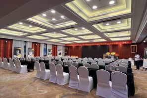 A conference room with rows of tables and chairs, a stage with a podium, and a person standing near the stage. - Chengcheng Huayuan Building (Chengcheng)