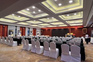 A conference room with rows of tables and chairs, a stage with a podium, and a person standing near the stage.