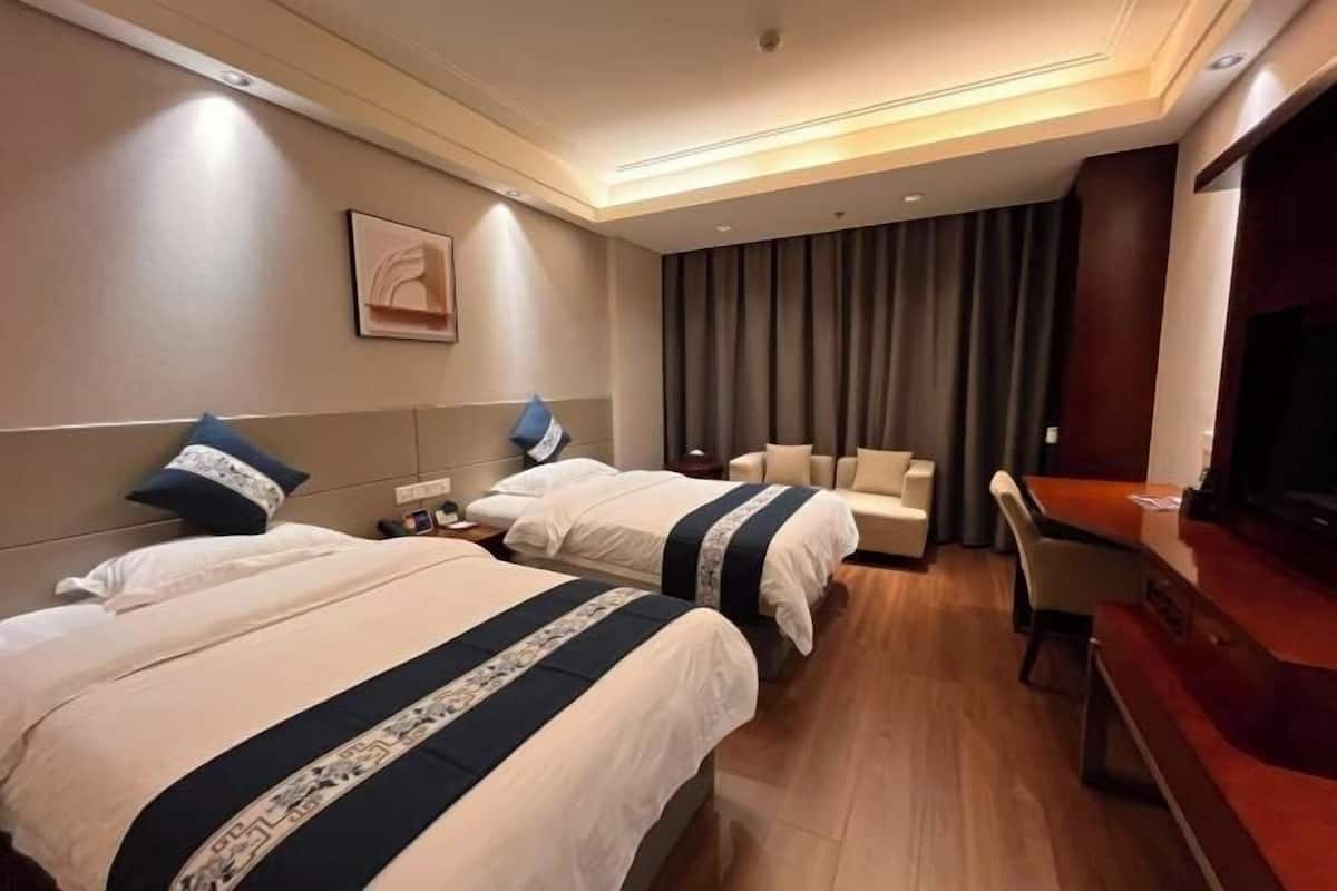 Ein Hotelzimmer mit zwei Betten, einem Sofa, einem Fernseher und einem Holztisch.