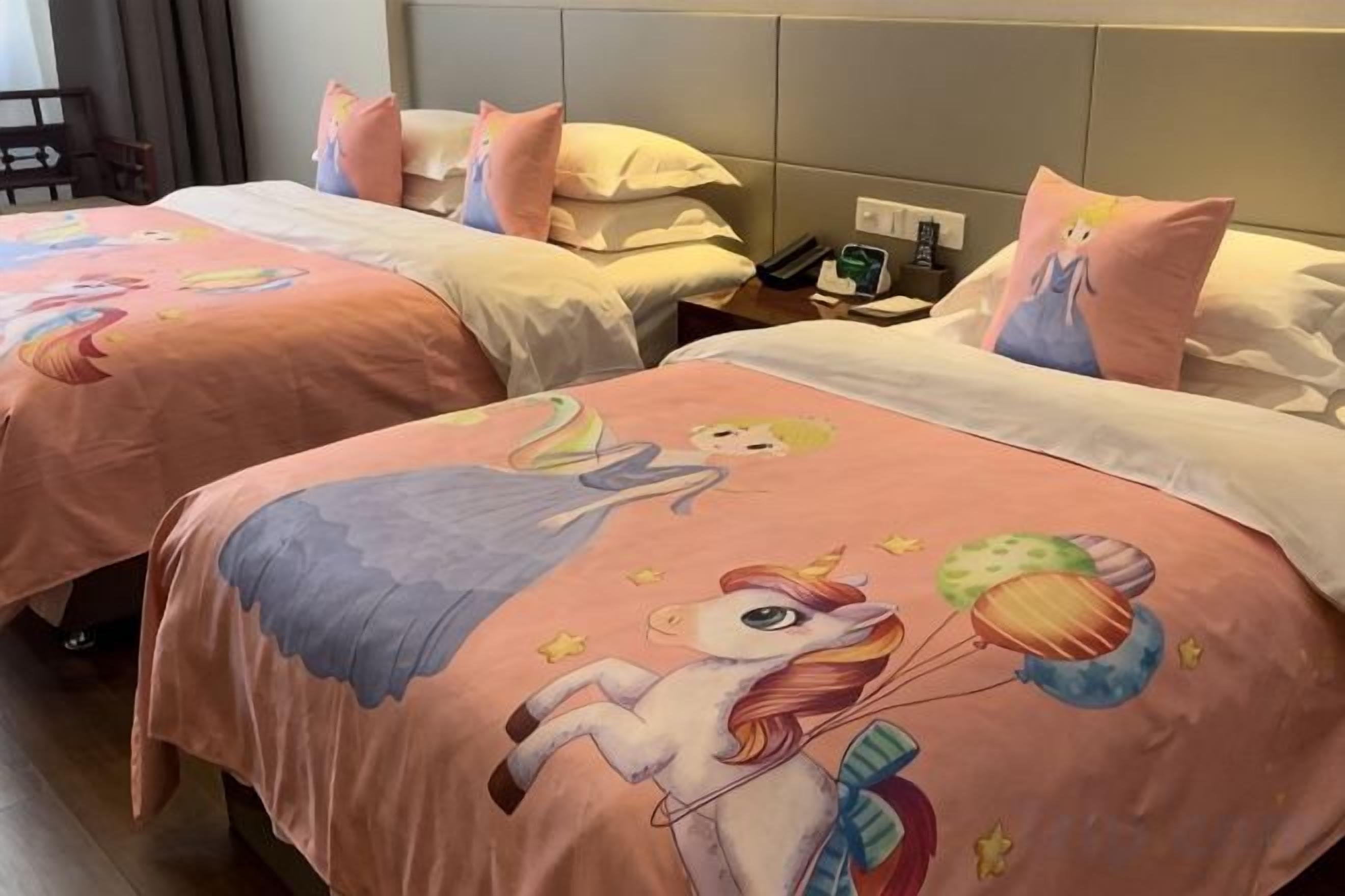 Two beds with pink bedding and cartoon characters, a bedside table with a phone, and a nightstand with a lamp.