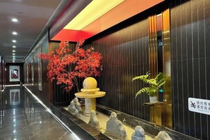 Un vestíbulo de hotel con una recepción, una fuente decorativa y una hilera de estatuas de piedra.