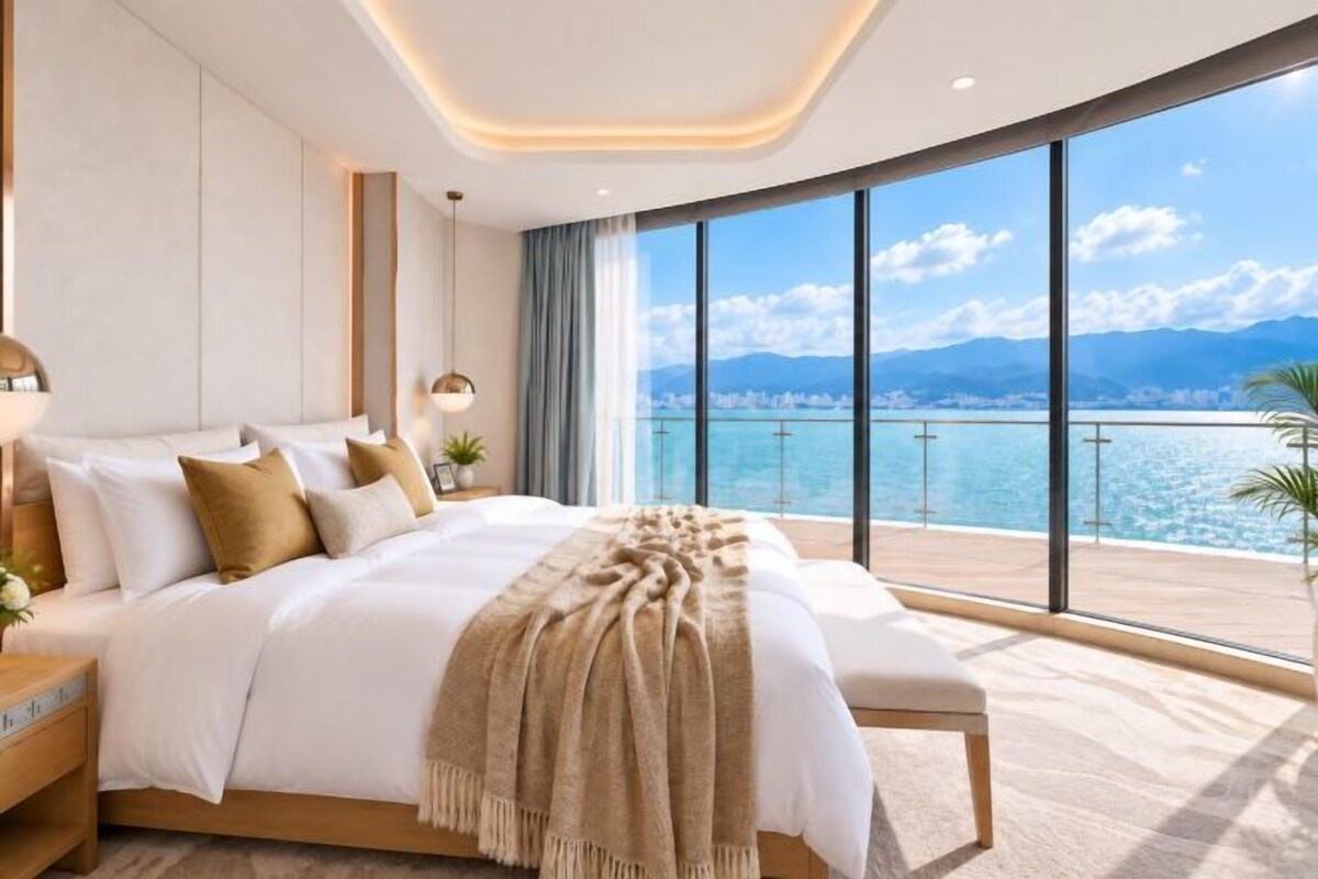 A modern bedroom with a large bed, a nightstand, and a view of the sea.