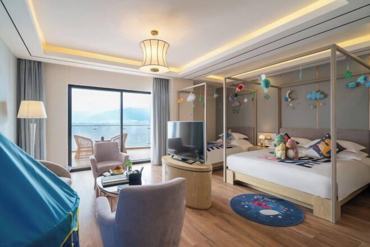 A modern hotel room with a balcony, a TV, a bed with plush pillows, and a round rug.