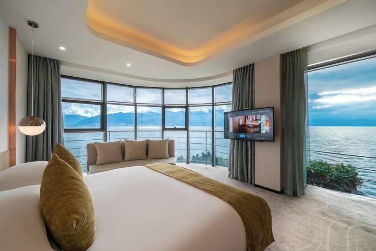 A modern hotel room with a large bed, a television, and a view of the sea.