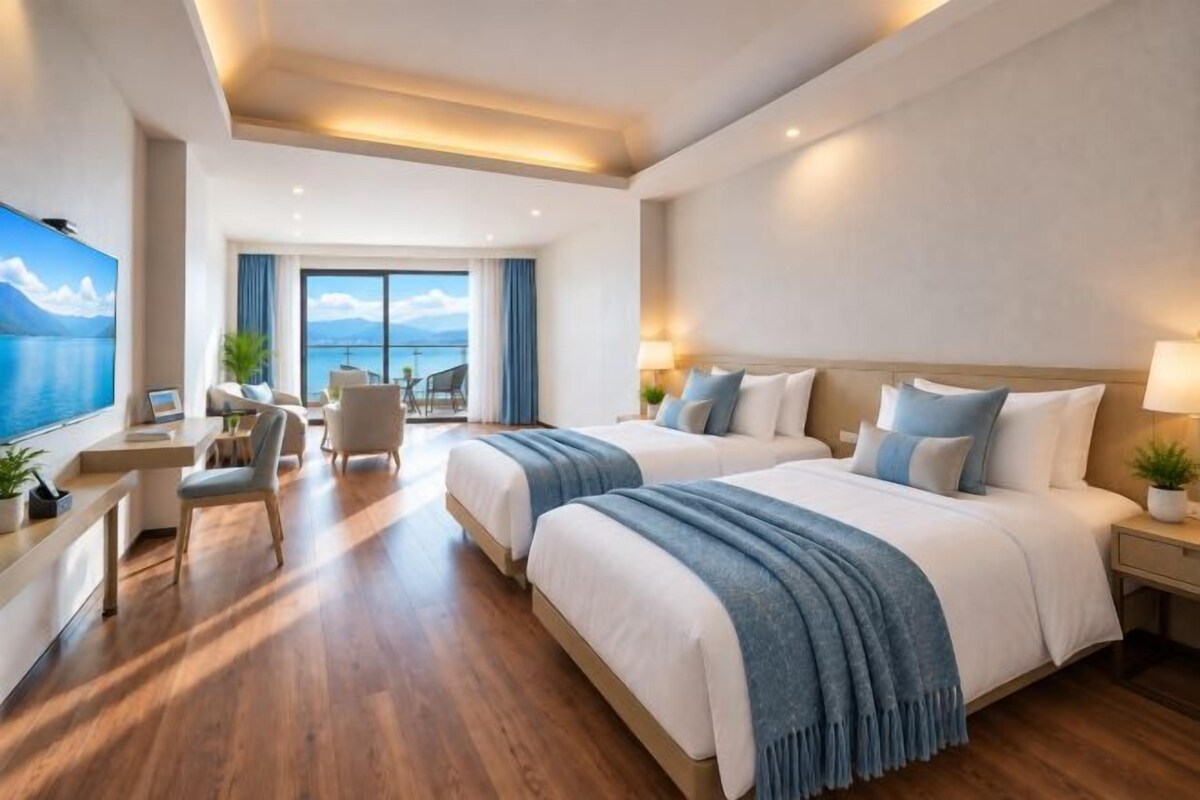 A hotel room with two beds, a desk, and a view of the sea.