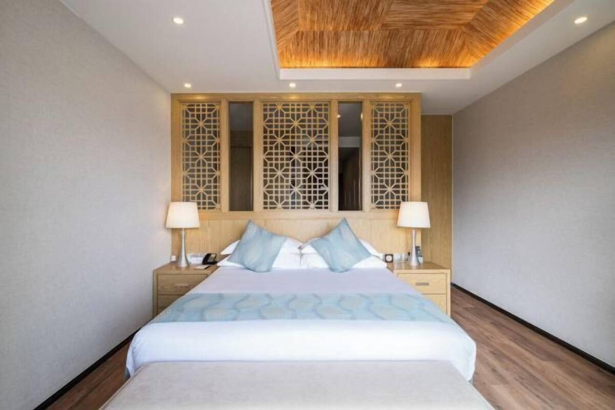A modern hotel room with a large bed, wooden headboard, and decorative panels.