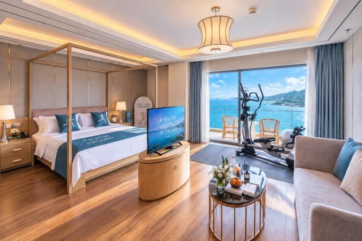 A hotel room with a four-poster bed, a television, a sofa, and a view of the sea.